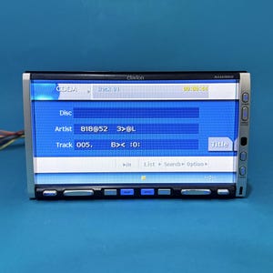 Può includere: Autoradio Clarion con schermo blu che mostra le informazioni della traccia. Lo schermo mostra il numero della traccia, l'artista e il tempo trascorso. Cornice argentata con pulsanti sui lati e in basso. Il modello MAX678RVD è visibile.