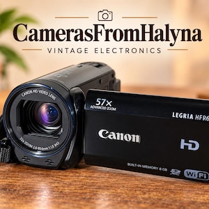 May include: A black Canon Legria HFR67 camcorder featuring a 57x advanced zoom lens, 8GB built-in memory, Wi-Fi capability, and HD recording. The device displays the text CamerasFromHalyna VINTAGE ELECTRONICS above the camera body.