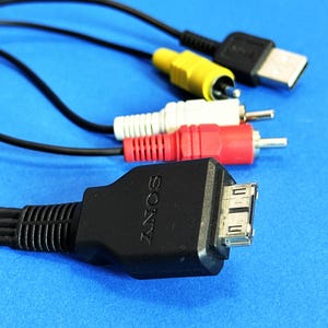 Puede incluir: Primer plano de varios cables electrónicos negros, amarillos, rojos y blancos sobre un fondo azul. Los cables incluyen USB, RCA y un conector de la marca Sony. Los conectores están enfocados, mostrando sus diferentes formas y colores.