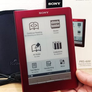 Puede incluir: Lector de libros digital Sony PRS-600 rojo con pantalla táctil que muestra opciones de menú. La pantalla muestra iconos de libros, notas y escritura a mano. El dispositivo se sostiene en una mano, con una funda negra y una caja en el fondo.