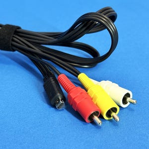 Puede incluir: Cable AV negro con un conector negro y conectores RCA rojos, amarillos y blancos. El cable está enrollado y asegurado con una correa de velcro negra. Los conectores están sobre un fondo azul.