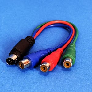 May include: An S-video cable with a black connector and a multi-coloured RCA cable. The RCA cables are red, blue, and green. The connectors have gold-coloured tips. The background is blue.
