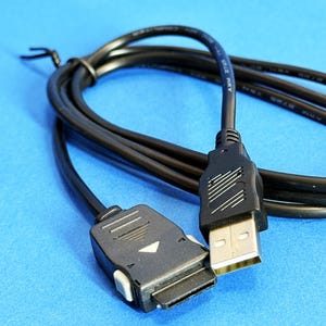 May include: Black USB cable with a rectangular connector and a USB-A connector. The cable is coiled and lies on a blue surface. The connectors are black with white accents.