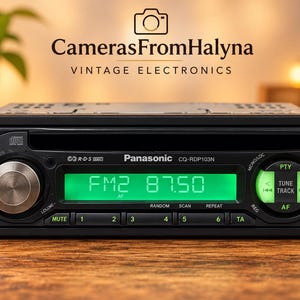 May include: A black Panasonic CQ-RDP103N car stereo head unit with a bright green digital display showing FM2 87.50. The device features a central volume knob, a CD slot, and various control buttons labeled Band, PTY, Tune, Track, Mute, and numbers 1 through 6.