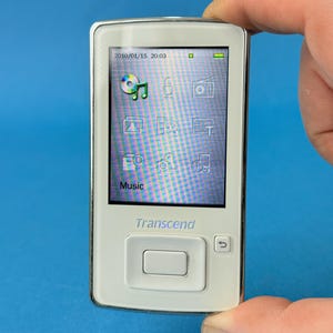 May include: A white Transcend MP3 player with a screen displaying a music interface. The device has a silver trim and a large central button. The screen shows the date and time, along with various icons. The device is held against a blue background.