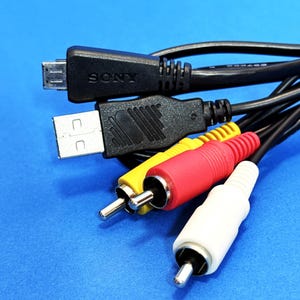May include: A selection of black cables with different connectors, including USB, RCA, and a micro USB with "SONY" printed on it. The RCA connectors are red, yellow, and white. The background is a solid blue.
