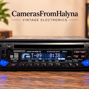 May include: A black Kenwood KDC-M4524G car stereo head unit featuring a digital display showing T-09 and 0:38, a CD slot, multiple control buttons, and two blue illuminated buttons on the left and right sides of the front panel interface.