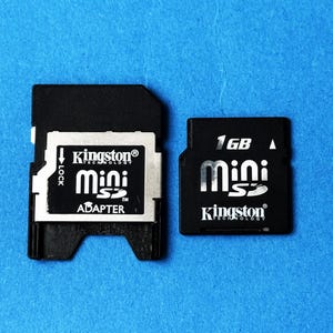 May include: Two black Kingston Mini SD cards on a blue background. One card is an adapter with the text "mini SD ADAPTER". The other card is labeled "1GB mini SD Kingston TECHNOLOGY".