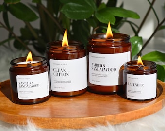 May include: Four amber glass candle jars with wooden wicks. The candles are labeled "Vanilla & Sandalwood", "Clean Cotton", "Amber & Sandalwood", and "Lavender".