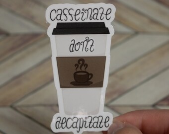 May include: A white sticker in the shape of a coffee cup with the words "caffeinate don't decapitate". The sticker has a black lid, a brown coffee sleeve, and a brown coffee cup graphic with steam.