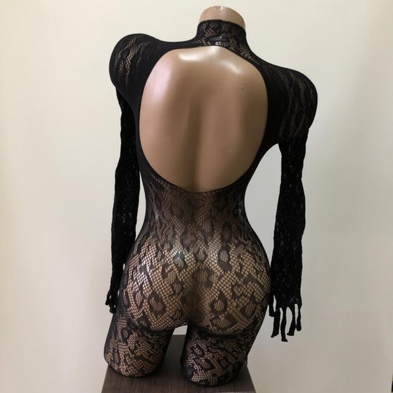 Puede incluir: Body de encaje negro con mangas largas y cuello alto. La espalda presenta un gran recorte en forma de ojo de cerradura. El body es ajustado y cubre las piernas. El encaje tiene un patr&oacute;n texturizado.