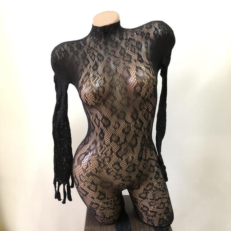 Puede incluir: Body de encaje negro con cuello alto y mangas largas. El body presenta un estampado de piel de serpiente y se exhibe en un maniqu&iacute;. La prenda est&aacute; dise&ntilde;ada para ser ajustada y est&aacute; hecha de un material transparente.