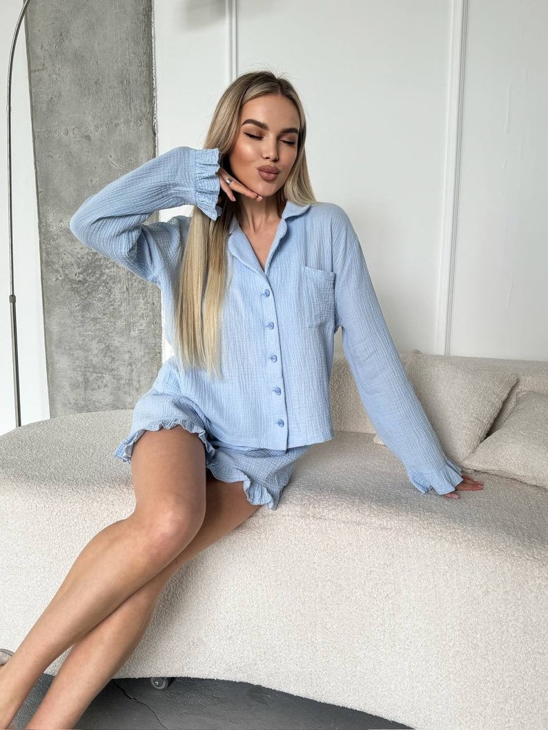 May include: A light blue pajama set with a button-up top and ruffled shorts. The top has a pocket on the left side.