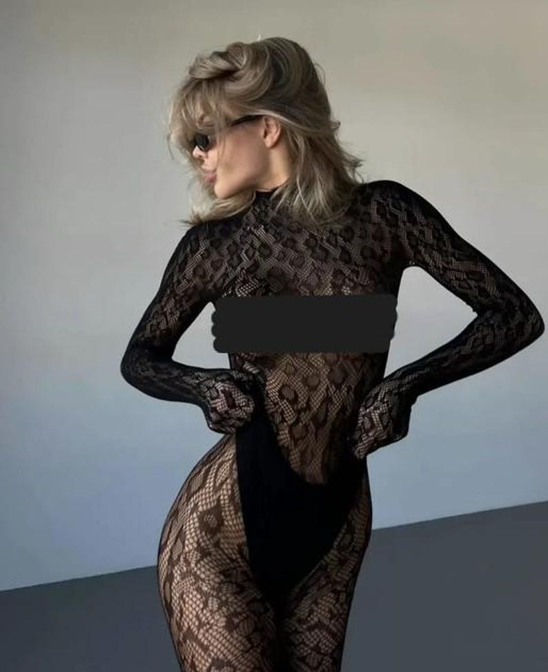 Puede incluir: Body de encaje negro con mangas largas y cuello alto. El body presenta un patr&oacute;n floral detallado y una parte inferior negra lisa. La modelo lleva gafas de sol y tiene el pelo rubio.