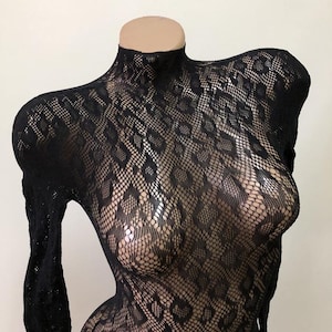 Puede incluir: Body negro de manga larga con cuello alto. La tela transparente presenta un patr&oacute;n texturizado en forma de diamante. La prenda se exhibe en un maniqu&iacute;.