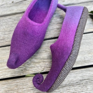 May include: Purple felt slippers with pointed toes and curled up heels. The slippers have a gradient color from light purple to dark purple.