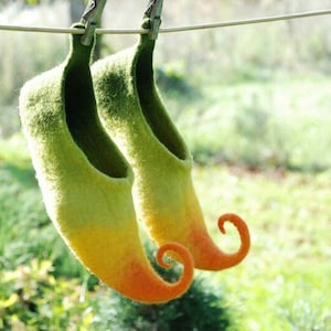 May include: A pair of green, yellow, and orange felt slippers with pointed toes and curled up heels. The slippers are hanging on a clothesline.