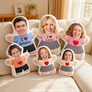 May include: Six custom-shaped plush cushions featuring printed photographic faces of individuals on cartoon-style bodies. The figures wear shirts with heart graphics and text including Amelia, Lucas, and BFF, paired with shorts or skirts.