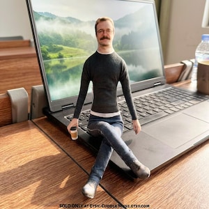 May include: A custom fabric doll featuring a realistic printed face of a person with glasses and a moustache, wearing a dark grey long-sleeve sweater, a white undershirt, and blue jeans. The doll holds a small coffee cup and sits on a laptop.