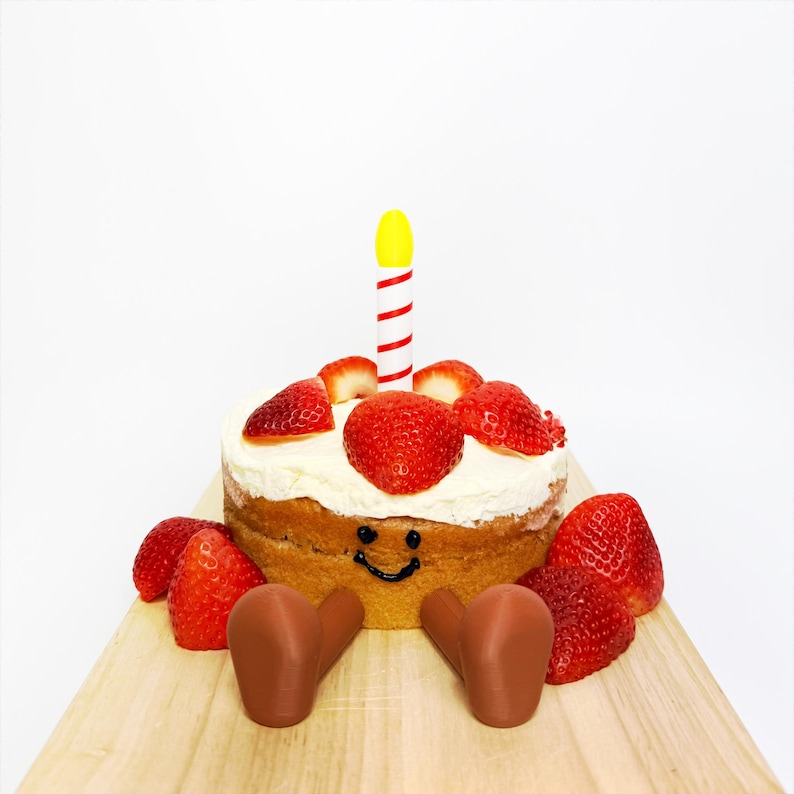 May include: A small round cake decorated with fresh strawberries and a single candle. The cake has a smiling face drawn on it and is surrounded by more strawberries. The cake is on a wooden board.