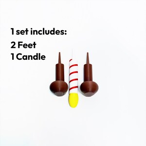 May include: A set of three decorative items, including two brown feet and one white candle with red stripes and a yellow base. The text "1 set includes: 2 Feet 1 Candle" is displayed.