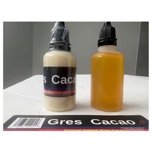 May include: Two clear bottles with black caps. One bottle contains a beige liquid, the other an orange liquid. A label at the bottom reads "Gres Cacao". The bottles are on a white surface.