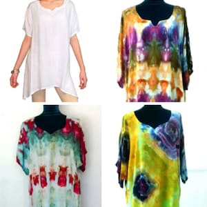 Op de afbeelding: Vier tunieken worden getoond. Eén is wit met een V-hals en korte mouwen. De andere drie zijn tie-dye met een V-hals en korte mouwen. De tie-dye tunieken hebben levendige kleuren, waaronder paars, oranje, geel, groen en rood.