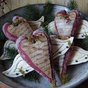 Könnte beinhalten: Fünf handgefertigte Stoffherzen mit Flügeln, verziert mit Vintage-Schrift und einem schneeweißen Finish. Die Herzen sind rot und weiß und in einer Schüssel angeordnet.