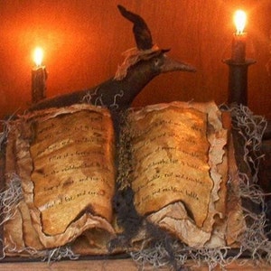 May include: An open book with aged, yellowed pages and handwritten text sits on a dark surface. A witch's hat with a long, curved beak sits on top of the book. Two lit candles are in the background, casting a warm glow on the scene.