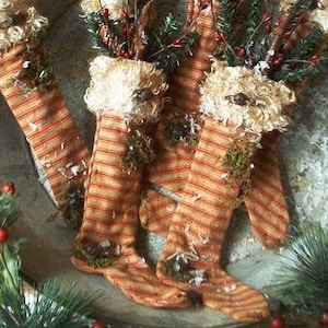Puede incluir: Tres calcetines a rayas con un aspecto rústico y vintage. Cada calcetín está decorado con un ribete blanco esponjoso y elementos naturales como musgo y ramitas.