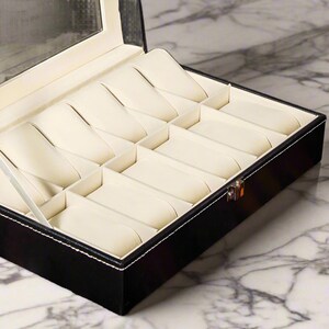 May include: Black leather watch box with a clear glass lid and 10 compartments for storing watches.