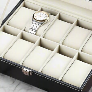 May include: Black leather watch box with a clear lid and 10 compartments lined with white velvet. The box is designed to hold and display watches.