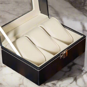 May include: Black leather watch box with a clear glass top and four white velvet watch cushions.