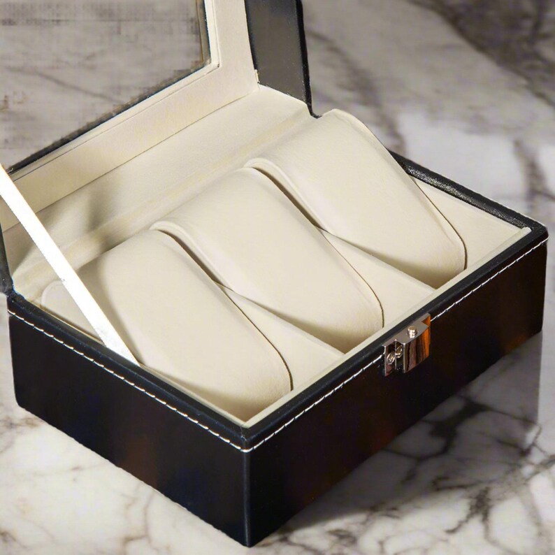 May include: Black leather watch box with a clear glass top and four white velvet watch cushions.