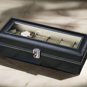 May include: Black leather watch box with a clear glass top. The box has a silver latch and is personalized with the name "Calvin Best Man".