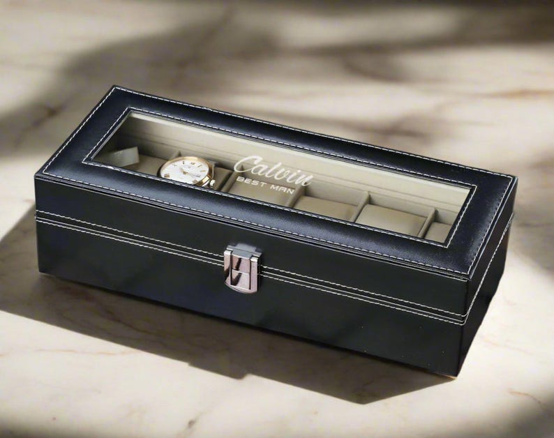 May include: Black leather watch box with a clear glass top. The box has a silver latch and is personalized with the name "Calvin Best Man".