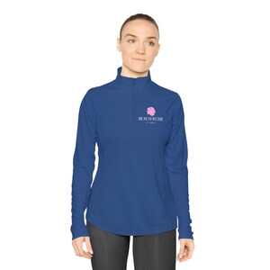 Op de afbeelding: Een koninklijkblauw longsleeve shirt met een kwart rits. Het shirt heeft een roze bloemenlogo met de tekst "Beachrose by Jeanne" op de linker borst.