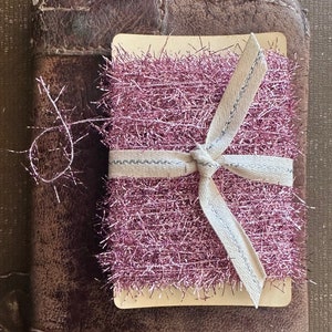 May include: A pink and white tinsel ribbon with a white satin ribbon tied around it. The ribbon is on a brown leather background.