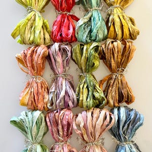May include: An overhead shot of a collection of colorful, tied ribbon bundles. The ribbons are in various shades of red, yellow, green, blue, and orange. Each bundle is tied with a silver-colored wire. The ribbons appear to be made of a soft, textured material.