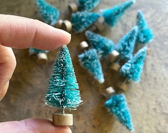 May include: A collection of miniature teal blue bottle brush Christmas trees with brown wooden bases.