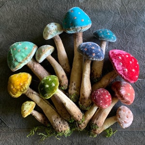 May include: A collection of 13 velvet mushroom ornaments in various colors, including teal, blue, green, red, yellow, and pink. The mushrooms are arranged in a cluster, with their stems pointing in different directions.