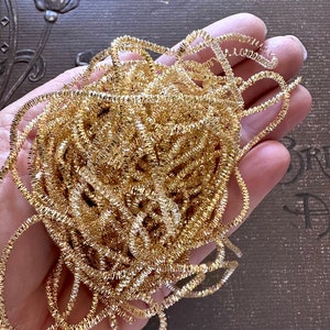 May include: A large amount of gold metallic tinsel, also known as icicle trim, is piled in a hand. The tinsel is shiny and has a slightly textured surface.