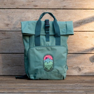 Peut inclure: Un sac à dos vert sarcelle avec un rabat supérieur et des bretelles réglables. Le sac à dos a une poche zippée à l'avant et un logo qui dit "Keep Earth Wild" avec un graphique de montagne et de soleil.