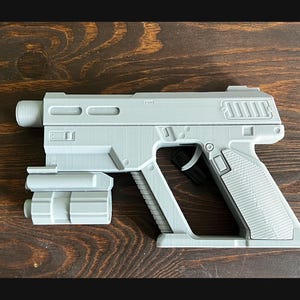 Peut inclure: Un jouet pistolet en plastique gris avec une extension de canon. Le pistolet a une poignée texturée et une gâchette noire.