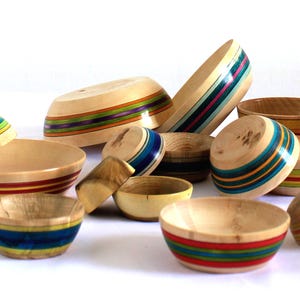 Peut inclure: Un ensemble de bols en bois avec des rayures colorées. Les bols sont en bois et de différentes tailles et couleurs. Les bols sont disposés en groupe sur une surface blanche.