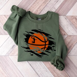 May include: A green sweatshirt with a distressed graphic of an orange basketball with a silhouette of a player dunking.