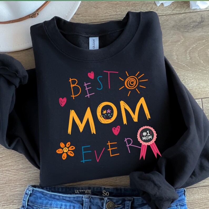 May include: Black sweatshirt with a colorful graphic that says "Best Mom Ever" with a sun, flowers, and hearts. A pink ribbon with a gold circle that says "#1 Mom" is on the bottom right.