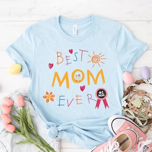 May include: Light blue t-shirt with the text "Best Mom Ever" in colorful letters. The shirt also features a sun, flowers, hearts, and a red ribbon with the text "#1 Mom".