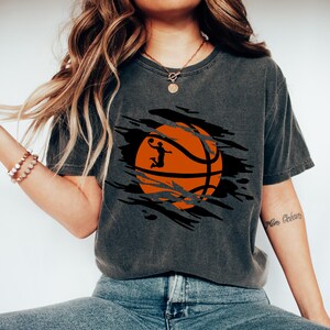 May include: A dark gray t-shirt with a graphic of a basketball with a player shooting a hoop. The basketball is orange and black and the player is a silhouette. The graphic is in a ripped or torn design.