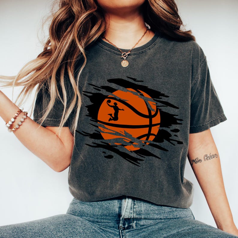 May include: A dark gray t-shirt with a graphic of a basketball with a player shooting a hoop. The basketball is orange and black and the player is a silhouette. The graphic is in a ripped or torn design.